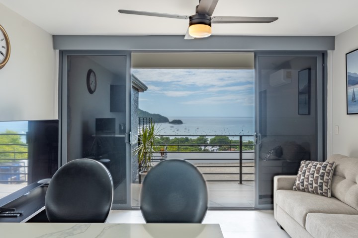 Modern living room with ocean view, sofa, TV, clock, and ceiling fan.