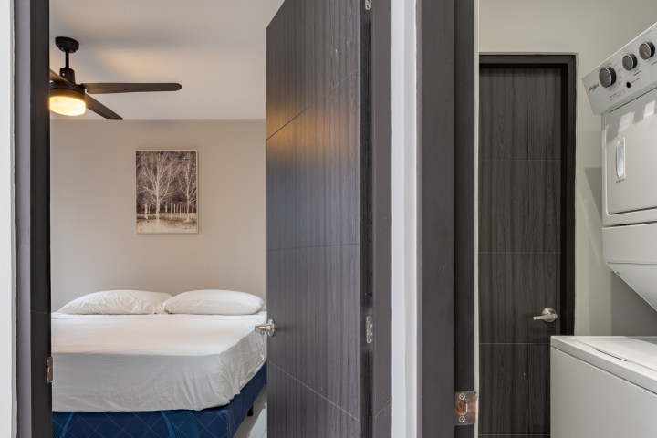 Open doors reveal a bedroom with a bed and a laundry area with stacked washer and dryer.