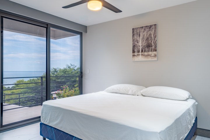 Minimalist bedroom with large window, bed, and a nature painting.