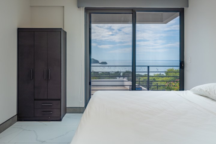Minimalist bedroom with bed, wardrobe, and ocean view balcony.