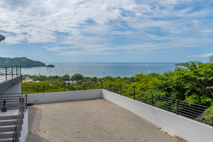 Ocean view from a terrace with greenery and blue sky.