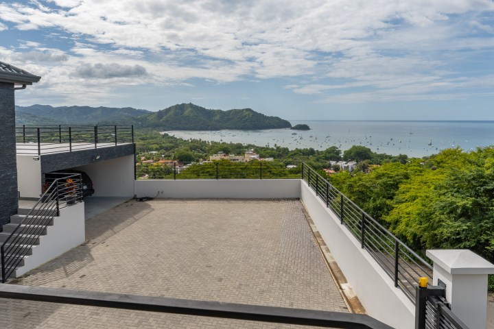 Rooftop terrace with ocean and mountain view, sunny sky.