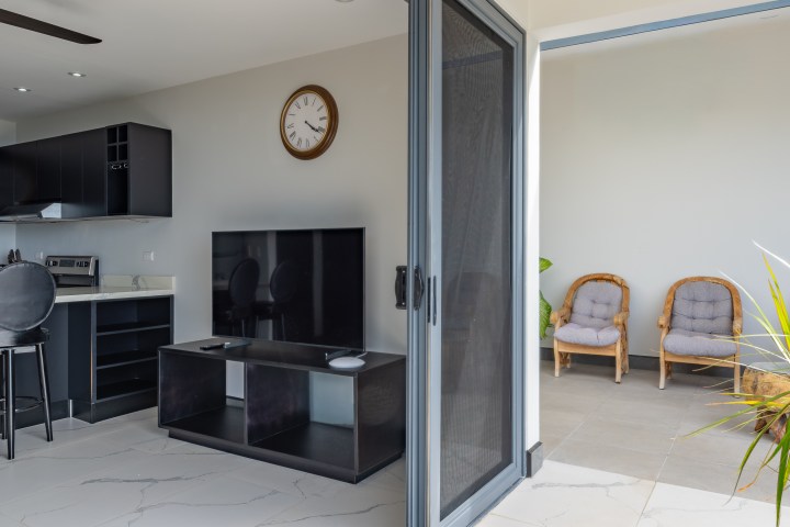 Modern living room with TV, kitchen, and patio chairs visible.