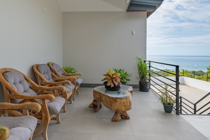 Patio with wooden chairs, small table, potted plants, and ocean view.