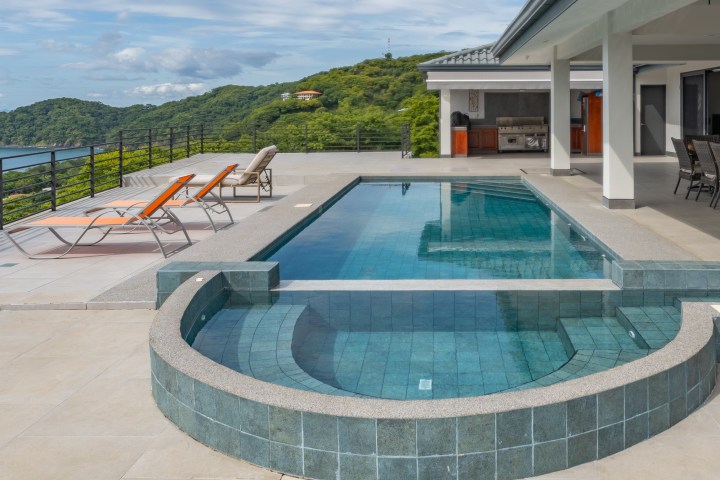 Modern villa with pool overlooking lush green hills and ocean view.