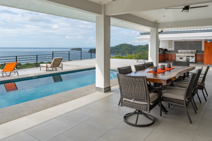 Outdoor patio with dining table, pool, and ocean view.
