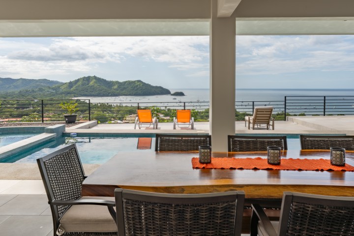 Luxurious patio with dining table, pool, and ocean view in the background.