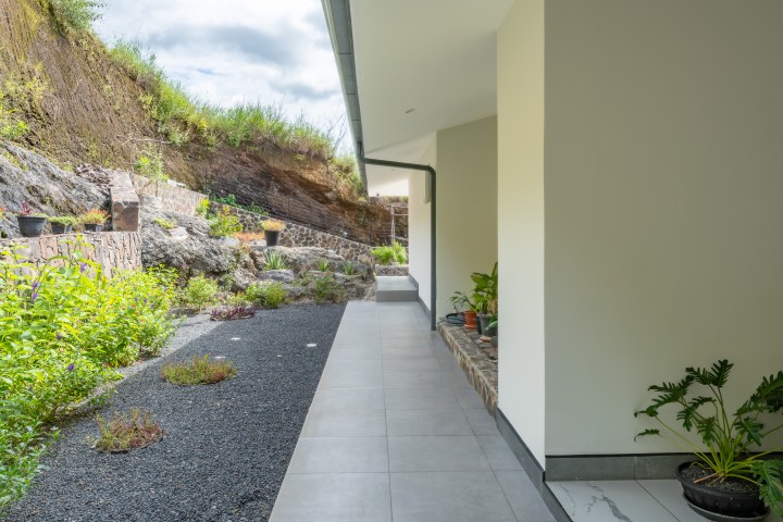 Outdoor covered walkway with plants on both sides and a rocky embankment.