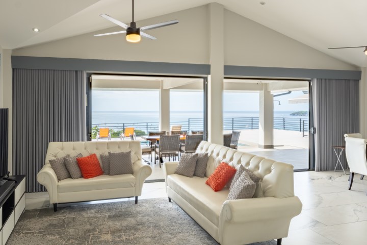 Modern living room with white sofas, ocean view, and open sliding doors.