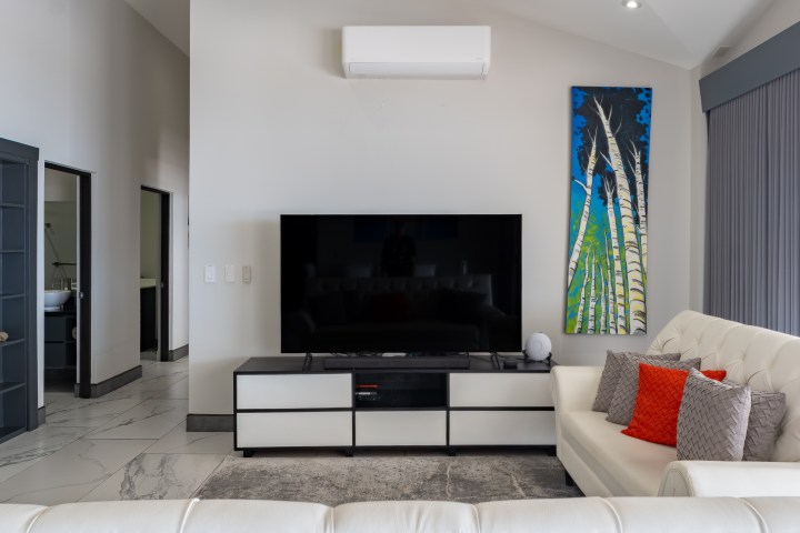 Modern living room with TV, white sofa, and colorful palm tree artwork.
