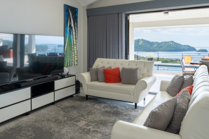 Modern living room with two white sofas, TV, and ocean view.