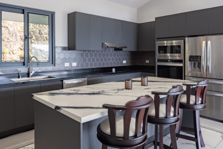 Modern kitchen with dark cabinets, marble island, and stainless steel appliances.