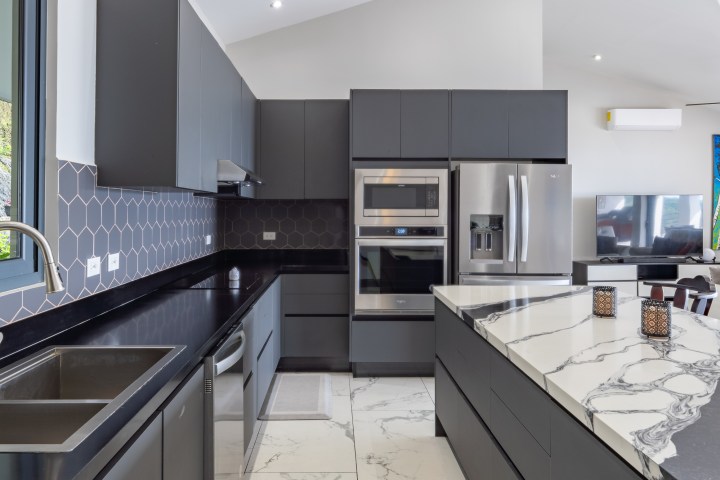 Modern kitchen with dark cabinets, marble island, and stainless steel appliances.