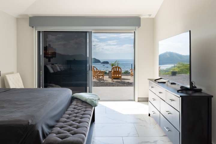Modern bedroom with ocean view, sliding glass doors, and outdoor seating area.