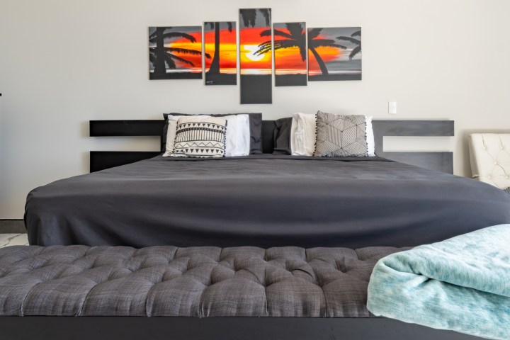 Modern bedroom with a gray bed, abstract sunset art, and a tufted bench.