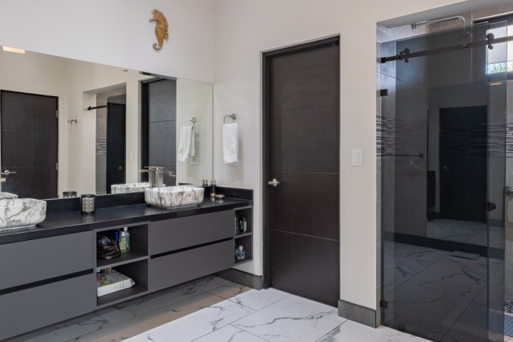 Modern bathroom with double sinks, large mirror, and glass shower door.