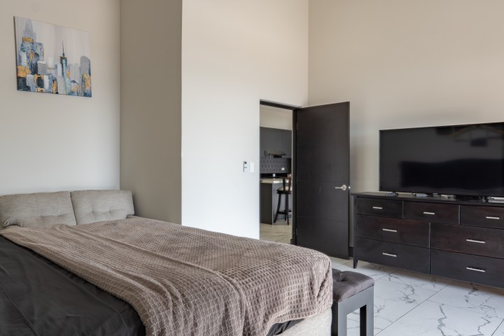 Modern bedroom with a bed, brown blanket, dresser, TV, and abstract wall art.