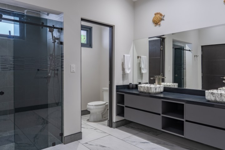Modern bathroom with double sinks, large mirror, and glass-enclosed shower.