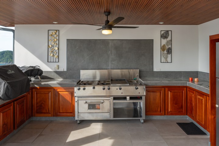 Outdoor kitchen with grill, wooden cabinets, and ceiling fan.