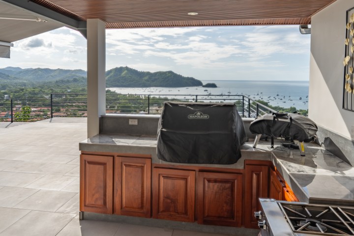 Outdoor kitchen with grill, overlooking ocean and hills.