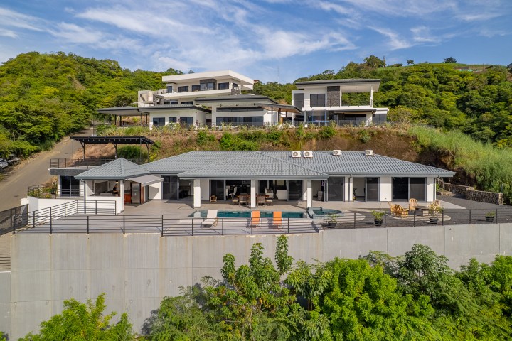 Modern hillside home with pool, surrounded by lush greenery.