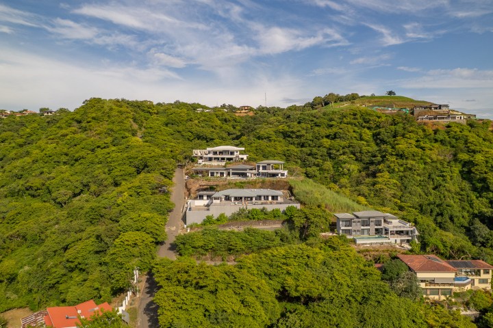 Hilltop houses surrounded by lush green trees under a blue sky.