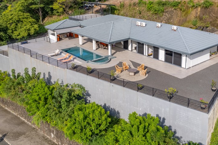 Elevated house with pool, deck chairs, and outdoor seating on concrete platform.