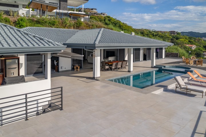 Modern patio with pool, sun loungers, and hillside view.