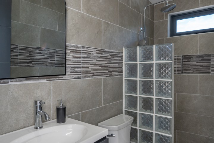 Modern bathroom with gray tile walls, glass block shower, and white sink.
