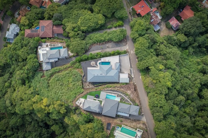 Aerial view of houses with pools surrounded by lush green trees.