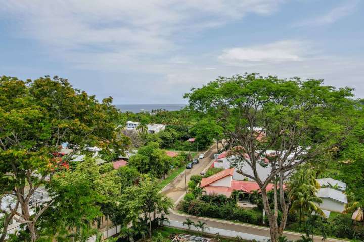 Lush green landscape with houses, trees, and distant sea view under a cloudy sky.