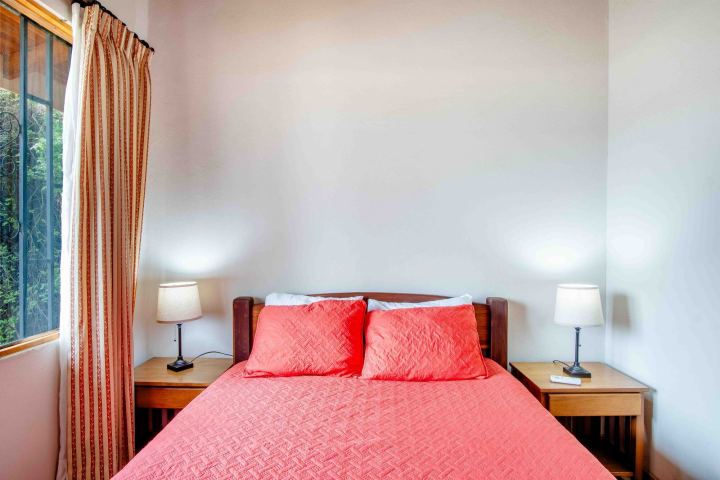 Bedroom with red bedding, two lamps on nightstands, and a window with curtains.