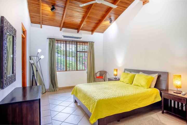 Bedroom with yellow bedspread, wooden ceiling, and lamps on side tables.