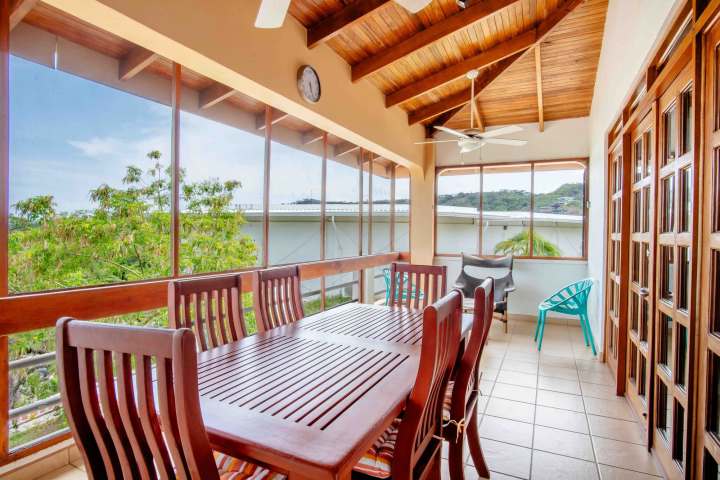 Bright sunroom with wooden dining set, ceiling fan, and large windows overlooking greenery.