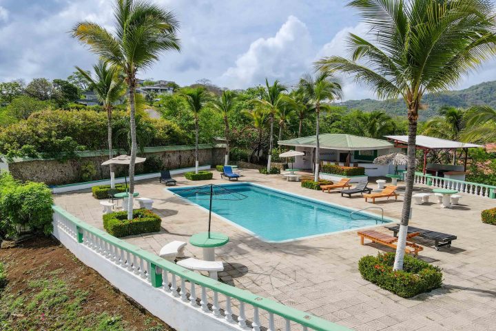 Pool area with loungers, umbrellas, and palm trees surrounded by lush greenery.