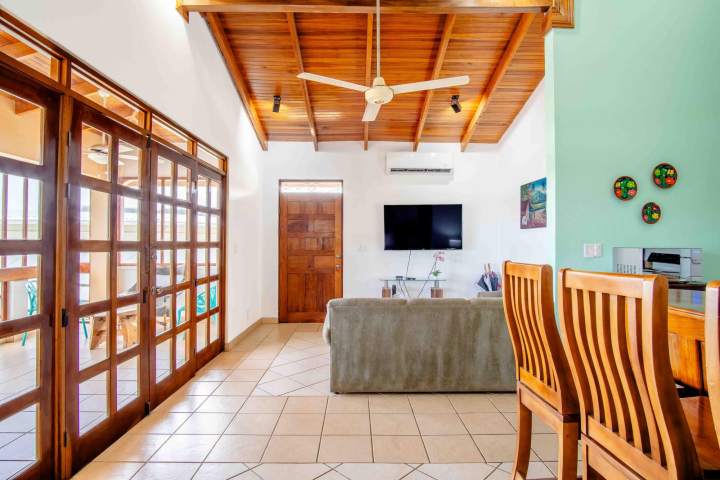 Living room with wooden ceiling, fan, sofa, TV, and glass doors.
