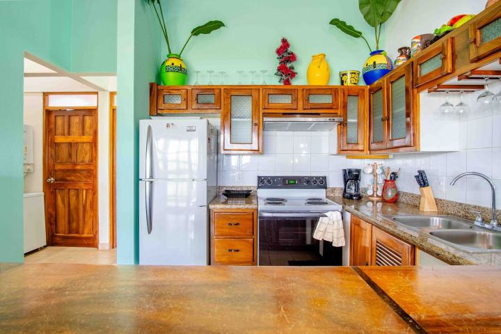 Bright kitchen with green walls, wooden cabinets, granite countertops, and decorative jars above cabinets.