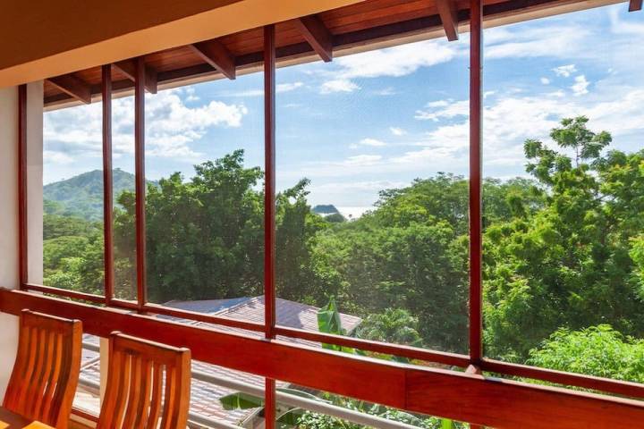 Large window overlooking trees and distant water view with blue sky.